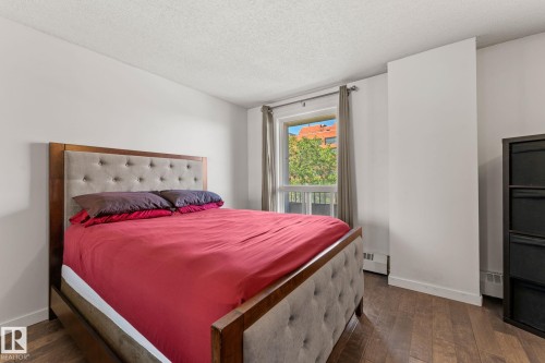 Bedroom featuring wood-finish flooring, white walls, and a window with an exterior building and tree visible - #503 10175 114 St Nw, Edmonton, AB - Indoor Photo Showing Bedroom