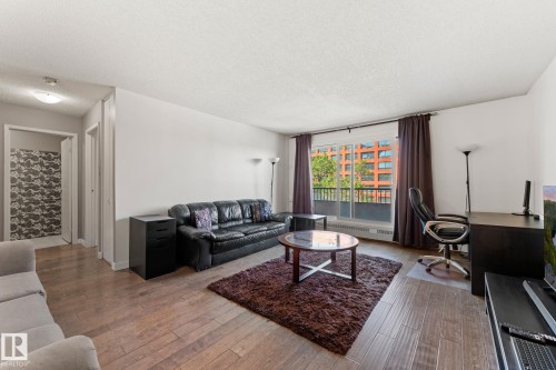 Spacious living area featuring wood-finish flooring, a large window with exterior balcony, and white walls - #503 10175 114 St Nw, Edmonton, AB - Indoor Photo Showing Living Room