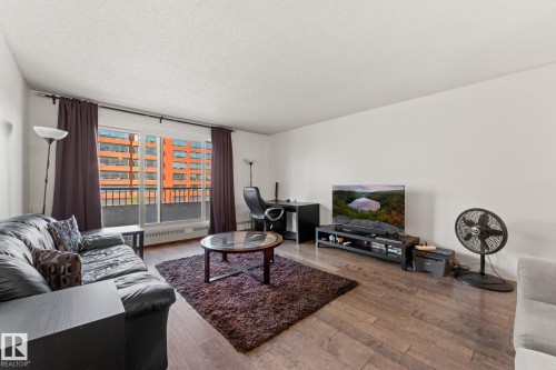 Living area featuring wood-finish flooring, white walls, and a large sliding glass door with a balcony - #503 10175 114 St Nw, Edmonton, AB - Indoor Photo Showing Living Room