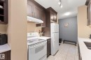 Kitchen featuring dark wood-finish cabinetry, white countertops, ceramic tile flooring, and white appliances including a refrigerator and electric range with an overhead exhaust fan - #503 10175 114 St Nw, Edmonton, AB  - Indoor Photo Showing Kitchen 
