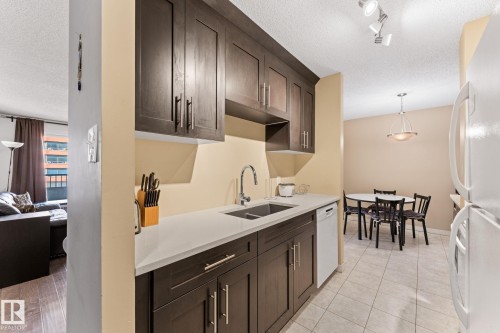 Kitchen featuring dark wood-finish cabinetry, light-toned countertops, a stainless steel sink, and track lighting - #503 10175 114 St Nw, Edmonton, AB - Indoor Photo Showing Kitchen With Double Sink