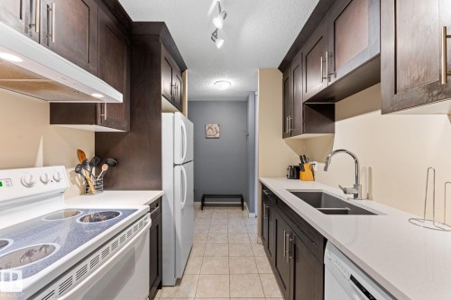 Galley kitchen featuring dark wood cabinetry, white countertops, and tile flooring - #503 10175 114 St Nw, Edmonton, AB - Indoor Photo Showing Kitchen With Double Sink