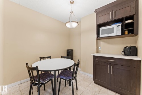 Built-in cabinetry with a white countertop and integrated shelving, featuring a microwave alcove, and neutral tile flooring - #503 10175 114 St Nw, Edmonton, AB - Indoor Photo Showing Dining Room