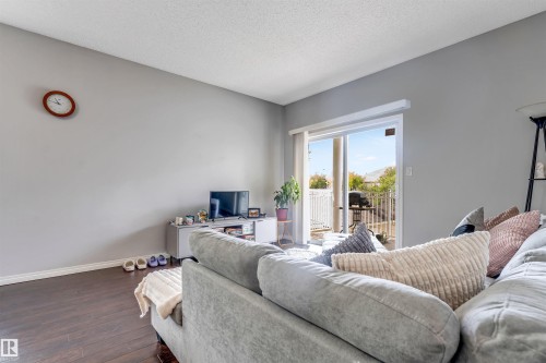Sliding glass patio door with white trim, dark wood-finish flooring, light gray wall paint, and white baseboards - #102 3040 Spence Wd Sw, Edmonton, AB - Indoor Photo Showing Living Room