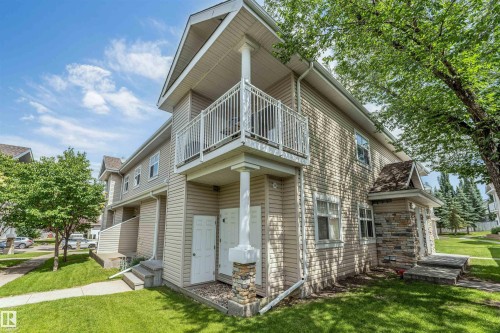 Multi-level exterior featuring light-toned siding, a second-story balcony with white railings, and stone veneer accents on the lower facade - #102 3040 Spence Wd Sw, Edmonton, AB - Outdoor With Balcony