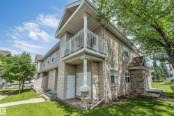Multi-level exterior featuring light-toned siding, a second-story balcony with white railings, and stone veneer accents on the lower facade - 
