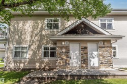 Multi-unit facade featuring horizontal vinyl siding, stone veneer accents, individual entry doors, and a second-story balcony with metal railings - 