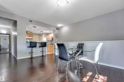 Open-concept kitchen and dining area featuring dark wood-finish flooring, light grey wall paint, and recessed lighting - #102 3040 Spence Wd Sw, Edmonton, AB - Indoor