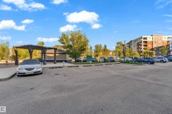 Paved parking area with a decorative wooden pergola structure and a residential building in the background - 