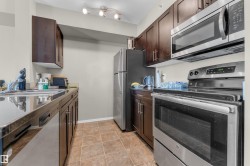 Kitchen featuring dark wood cabinetry, stainless steel appliances including a range and microwave, track lighting, and tile flooring - 