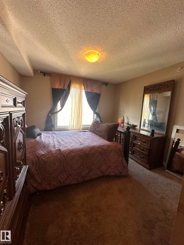 Wall-to-wall carpeting in a neutral tone, ceiling-mounted light fixture, and a window with curtain rod and drapes - #419 11808 22 Av Sw, Edmonton, AB - Indoor Photo Showing Bedroom