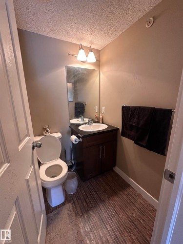Compact bathroom featuring a dark wood-finish vanity with an integrated sink, a wall-mounted mirror, and a two-bulb vanity light fixture - #419 11808 22 Av Sw, Edmonton, AB - Indoor Photo Showing Bathroom