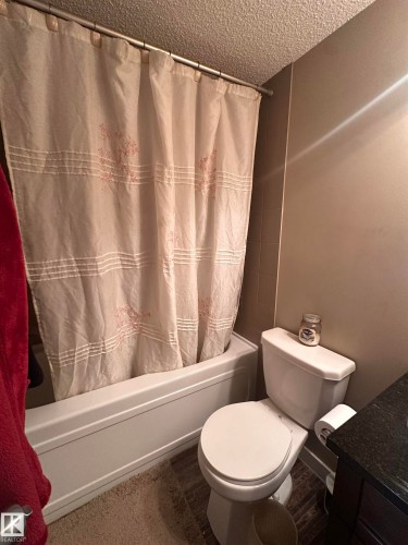 White porcelain tub, toilet, and dark wood-finish vanity with a dark countertop - #419 11808 22 Av Sw, Edmonton, AB - Indoor Photo Showing Bathroom