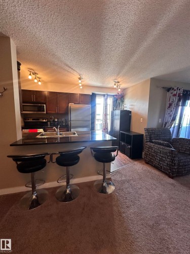 Kitchen featuring dark wood-finish cabinetry, stainless steel appliances, and track lighting - #419 11808 22 Av Sw, Edmonton, AB - Indoor