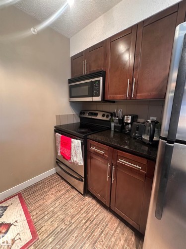 Full kitchen featuring dark wood cabinetry, stainless steel appliances, dark countertops, and wood-finish flooring - #419 11808 22 Av Sw, Edmonton, AB - Indoor Photo Showing Kitchen