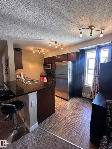 Contemporary kitchen featuring dark wood cabinetry, a double basin sink, and wood-finish flooring - #419 11808 22 Av Sw, Edmonton, AB - Indoor Photo Showing Kitchen With Double Sink