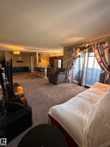 Open-concept living area with neutral carpeting and a sliding glass door - #419 11808 22 Av Sw, Edmonton, AB - Indoor