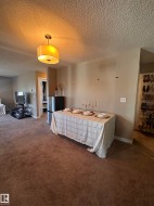 Expansive carpeted area with a modern drum pendant light fixture and neutral wall tones - 