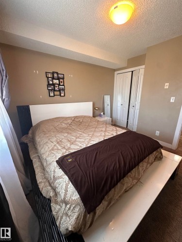 Spacious bedroom featuring neutral wall tones, a ceiling-mounted light fixture, and textured carpeting - #419 11808 22 Av Sw, Edmonton, AB - Indoor Photo Showing Bedroom