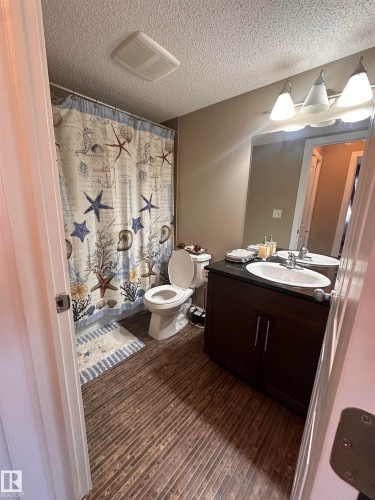 Bathroom featuring wood-finish flooring, a dark wood-finish vanity with a white oval sink, and a chrome faucet - #419 11808 22 Av Sw, Edmonton, AB - Indoor Photo Showing Bathroom