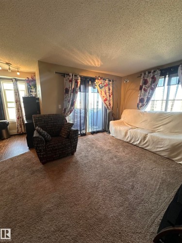 Spacious living area featuring neutral-toned carpeting, ample natural light from multiple windows, and a sliding glass door - #419 11808 22 Av Sw, Edmonton, AB - Indoor Photo Showing Other Room