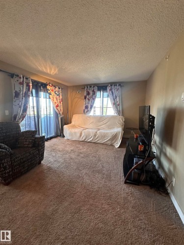 Carpeted living area featuring a neutral color palette, multiple windows, a sliding glass door, and textured ceilings - #419 11808 22 Av Sw, Edmonton, AB - Indoor Photo Showing Bedroom