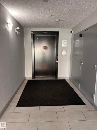 Elevator access with a textured black door, complemented by light grey tile flooring and a black floor mat - #419 11808 22 Av Sw, Edmonton, AB - Indoor Photo Showing Other Room