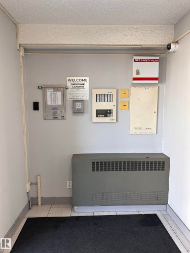 Entryway featuring a security camera, fire safety plan box, building information panel, and a wall-mounted heating unit - #419 11808 22 Av Sw, Edmonton, AB - Indoor Photo Showing Other Room