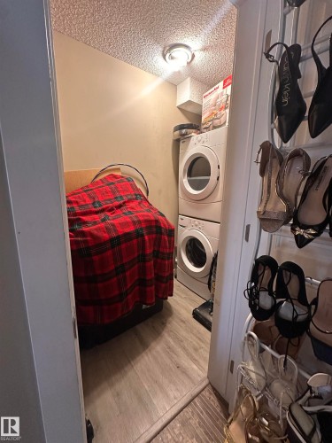 Dedicated laundry area featuring stacked appliances and wood-finish flooring - #419 11808 22 Av Sw, Edmonton, AB - Indoor Photo Showing Laundry Room