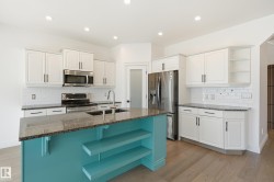 Kitchen featuring a turquoise island with integrated shelving, granite countertops, white cabinetry with dark hardware, stainless steel appliances, and wood-finish flooring - 