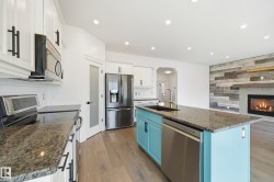 Kitchen featuring a turquoise island with a stainless steel sink and dishwasher, granite countertops, white cabinetry with black hardware, and wood-finish flooring - 