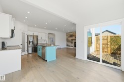 Open-concept interior featuring light wood-finish flooring, white cabinetry, a teal kitchen island with a built-in sink, and stainless steel appliances - 