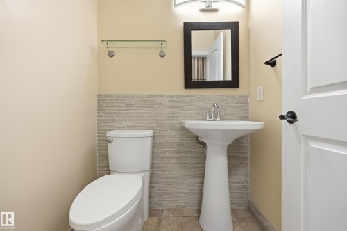 Bathroom featuring a pedestal sink, textured wall tiling, a contemporary rectangular mirror, and an arched vanity light fixture - 1 Southfork Close, Leduc, AB - Indoor Photo Showing Bathroom
