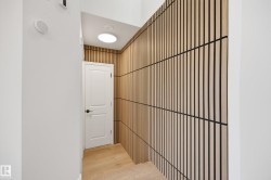 Modern hallway featuring a striking wood-slat accent wall, light wood-finish flooring, and crisp white painted walls - 