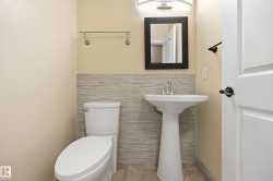 Bathroom featuring a pedestal sink, textured wall tiling, a contemporary rectangular mirror, and an arched vanity light fixture - 