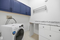 Laundry area featuring blue wall cabinetry with dark hardware, a white counter, and white base cabinets with silver hardware - 