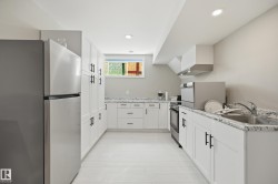 Contemporary kitchen featuring white cabinetry with matte black hardware, stainless steel appliances, and light-toned wood-finish flooring - 