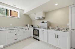 Kitchenette featuring white shaker-style cabinetry with matte black hardware, light-toned countertops, and light wood-finish flooring - 