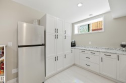 Kitchenette featuring extensive white shaker cabinetry with matte black hardware, light-toned countertops, wood-finish flooring, and a stainless steel refrigerator - 