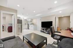 Open-concept living area featuring a compact kitchen, recessed lighting, neutral wall tones, light-toned flooring, and a built-in desk area - 