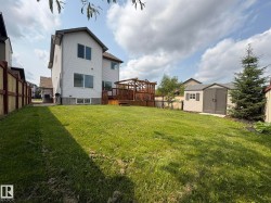 Expansive yard featuring a wooden privacy fence, a multi-level deck with a pergola, a mature evergreen tree, and a detached storage shed - 
