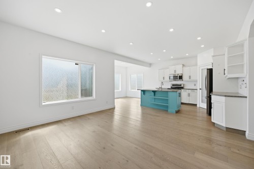 Open-concept living area featuring light wood-finish flooring, recessed lighting, and a kitchen with white cabinetry and a contrasting teal island - 1 Southfork Close, Leduc, AB - Indoor Photo Showing Kitchen