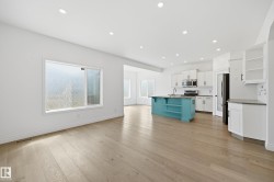 Open-concept living area featuring light wood-finish flooring, recessed lighting, and a kitchen with white cabinetry and a contrasting teal island - 