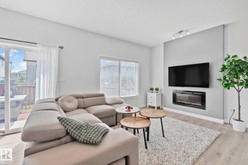 Living area featuring light wood-finish flooring, a wall-mounted electric fireplace, and a sliding glass door opening to an exterior deck - 249 39A Avenue, Edmonton, AB - Indoor Photo Showing Living Room With Fireplace