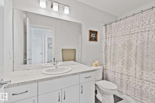 Bathroom featuring a spacious vanity with an undermount sink, a large wall-mounted mirror, white cabinetry, and a shower with tile surround - 249 39A Avenue, Edmonton, AB - Indoor Photo Showing Bathroom