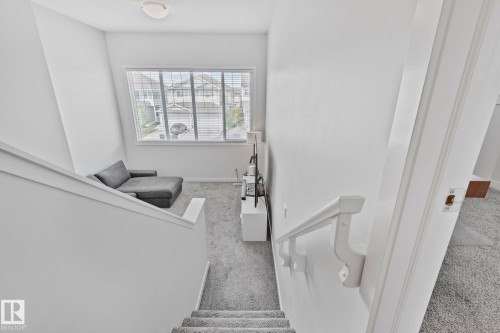 Carpeted staircase descending to a versatile landing area featuring a large window with horizontal blinds, overhead lighting, and a white handrail - 249 39A Avenue, Edmonton, AB - Indoor Photo Showing Other Room