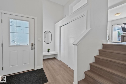 Bright entryway featuring a white paneled door with glass inserts, wood-finish flooring, a built-in white bench, and a white staircase with wood-finish treads - 249 39A Avenue, Edmonton, AB - Indoor Photo Showing Other Room