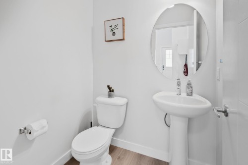 White pedestal sink with chrome faucet, circular frameless mirror, and wood-finish flooring - 249 39A Avenue, Edmonton, AB - Indoor Photo Showing Bathroom