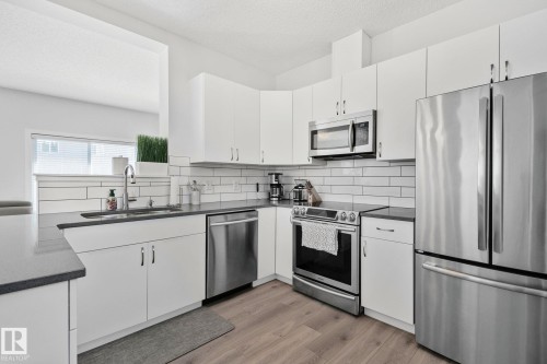 Contemporary kitchen featuring light wood-finish flooring, white cabinetry, dark countertops, a subway tile backsplash, and stainless steel appliances - 249 39A Avenue, Edmonton, AB - Indoor Photo Showing Kitchen With Upgraded Kitchen