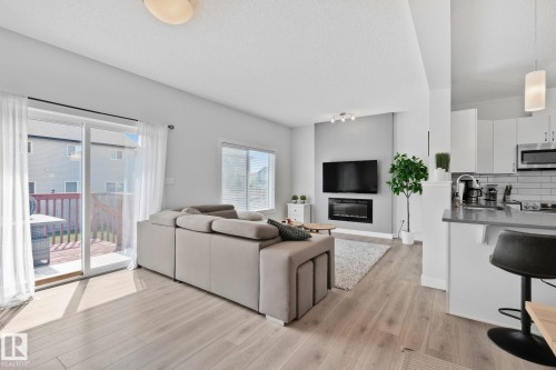 Open-concept living space featuring wood-finish flooring, a contemporary electric fireplace, and sliding glass doors to a wooden deck - 249 39A Avenue, Edmonton, AB - Indoor With Fireplace